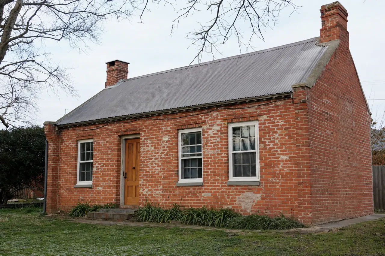 A single-storey old brick cottage with a pitched roof and a timber door — heritage plastering, Launceston. Illustrative example.